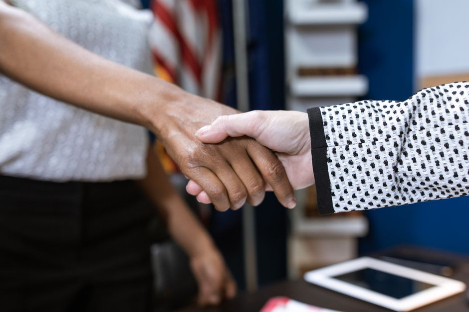 A real estate agent and a happy client shaking hands across a kitchen island in a bright, contemporary home, symbolizing a successful partnership and agreement on commission.